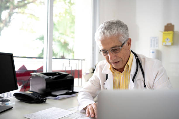 istock Senior male doctor using laptop at doctor's office 1201417191