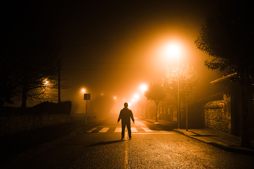 The silhouette of a young man standing in the middle of a road at night under thick fog
