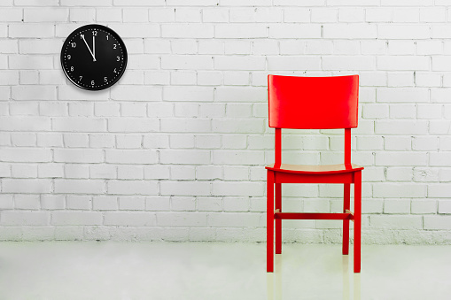 Red chair against white brick wall with clock