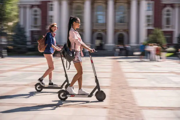 Young modern women riding e-scooters in the city in a warm autumn day