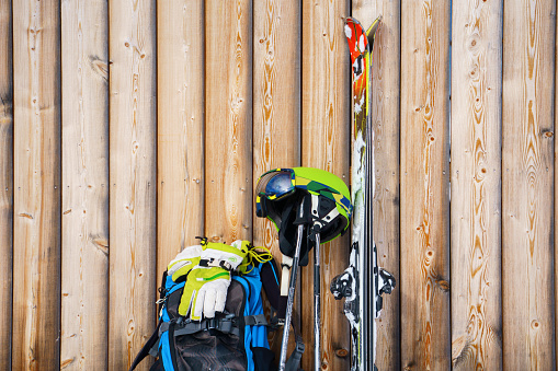 Skis, helmet, backpack at ski resort on background of wooden fence