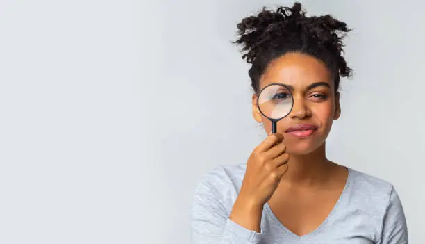 Photo of Curious girl holding magnifier over grey background