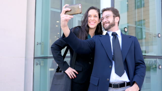 Attractive business couple take selfie with cell phone outside office building