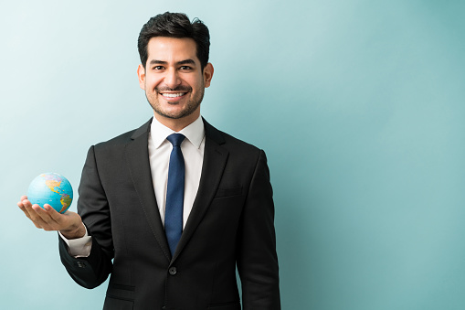 Portrait of smiling young male entrepreneur holding globe while standing against colored background