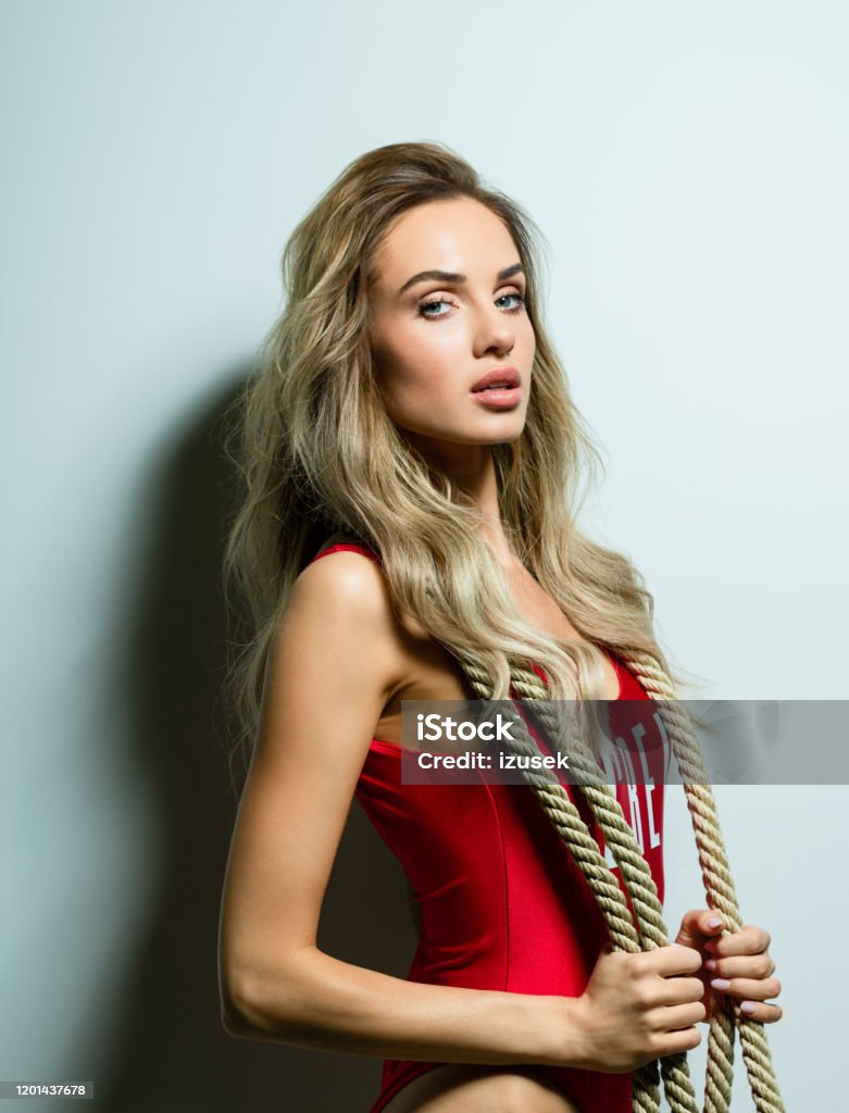 Glamour summer portrait of beautiful young woman Summer portrait of glamour blond long hair young woman wearing red swimsuit and holding rope. Standing against white background. Studio shot, one person. Adult Stock Photo