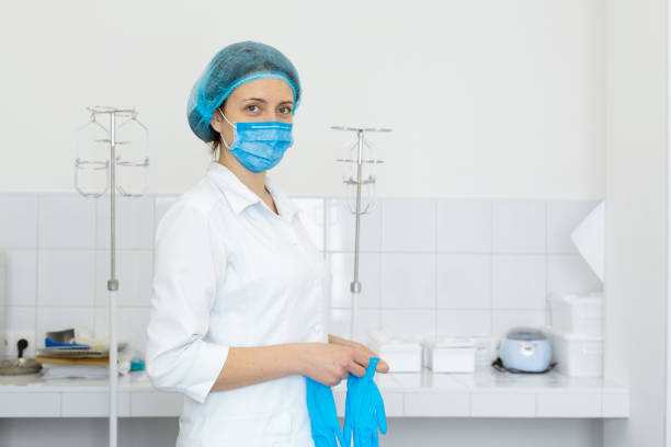 白いコートを着た看護師は、明るい取り扱い室で医療処置の前に手袋を着用します - lab coat nurse doctor female doctor ストックフォトと画像