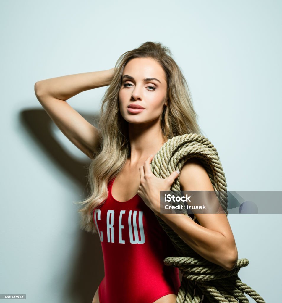 Glamour summer portrait of beautiful young woman Summer portrait of glamour blond long hair young woman wearing red swimsuit and holding rope on her shoulder. Standing against white background. Studio shot, one person. Adult Stock Photo