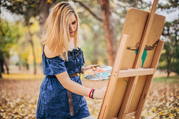 Young female artist is painting in nature on beautiful autumn day