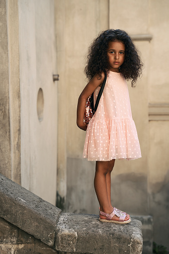 Adorable Mixed Race 4 Year Old Little Girl With Beautiful Thick Curly Black  Hair Wearing Pink Dress Sandals And A Backpack Standing On A Stone Edge In  Old City Street Stock Photo -