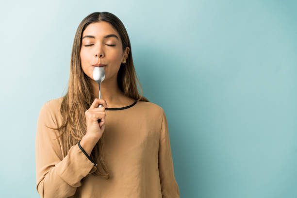 Young Woman Lost In Taste At Studio Hispanic young woman tasting spoon while standing over blue background ready to eat stock pictures, royalty-free photos & images