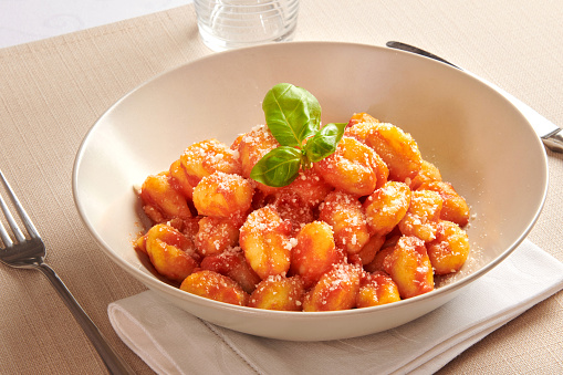 Serving of Italian gnocchi pasta in a bowl with pomodoro sauce and fresh basil on a folded napkin at table, a traditional regional Italian dish