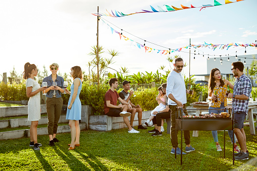 Family and friends enjoying Asado party on sunny day. Males and females are spending leisure time together. They are in backyard during summer.