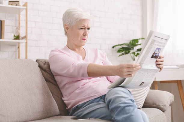 senior lady squinting and holding newspaper far from eyes - newspaper reading blank women imagens e fotografias de stock