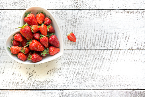 Ripe organic strawberry in plate as heart isolated on white wooden background. View from above.