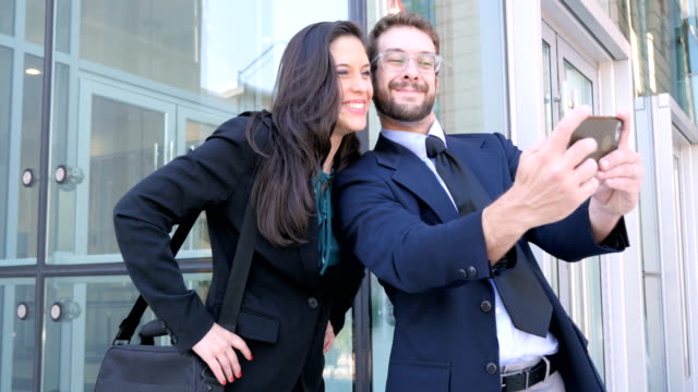 Well dressed man and woman take selfie with smart phone outside business complex