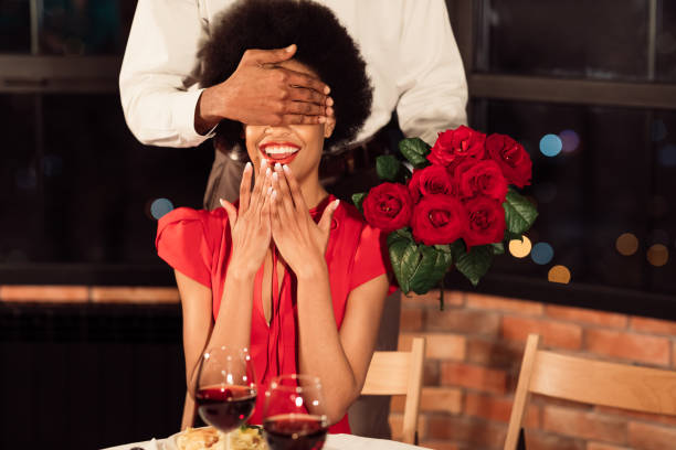 le petit ami couvrant les yeux de girlfriend retenant des roses ayant la date dans le restaurant - anniversary couple rose black photos et images de collection