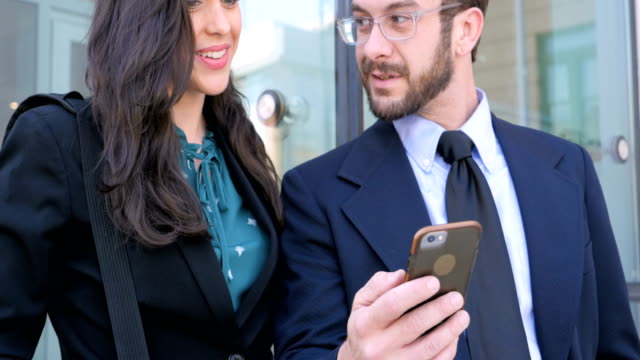 A well dressed man and woman looking at smart phone smiling and talking outside