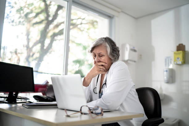 preocupado / cansado médico mayor usando computadora portátil en su oficina - old senior adult women tired fotografías e imágenes de stock