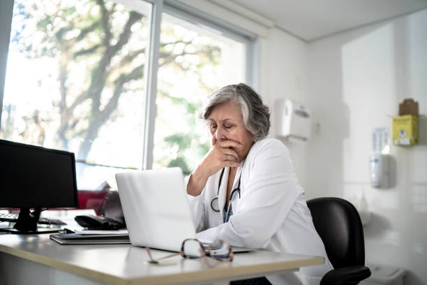 Worried / tired senior female doctor using laptop at her office Worried / tired senior female doctor using laptop at her office oops stock pictures, royalty-free photos & images