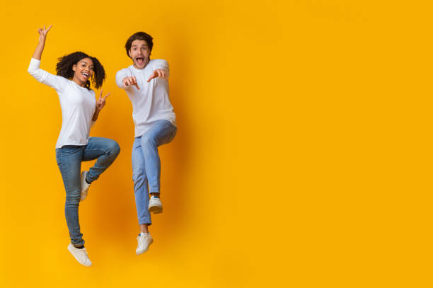istock Funny Interracial Couple Jumping In Air On Yellow Background In Studio 1201453193