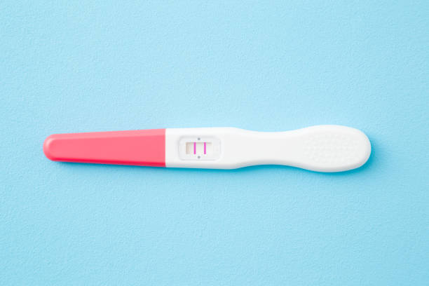istock Pregnancy test with two stripes on light blue table background. Pastel color. Positive result. Closeup. Top down view. 1201453518