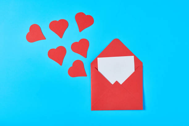 istock Red hearts near open postal envelope with blank white paper on blue desk. Love message. Concept of Valentines Day. Space for text. Top view 1201454238