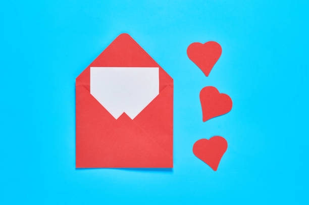 istock Red hearts near open postal envelope with blank white paper on blue desk. Love message. Concept of Valentines Day. Space for text. Top view 1201454244