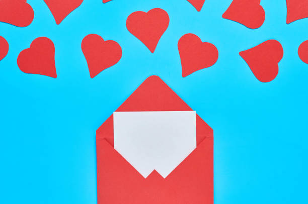 istock Red hearts near open postal envelope with blank white paper on blue desk. Love message. Concept of Valentines Day. Space for text. Top view 1201454245