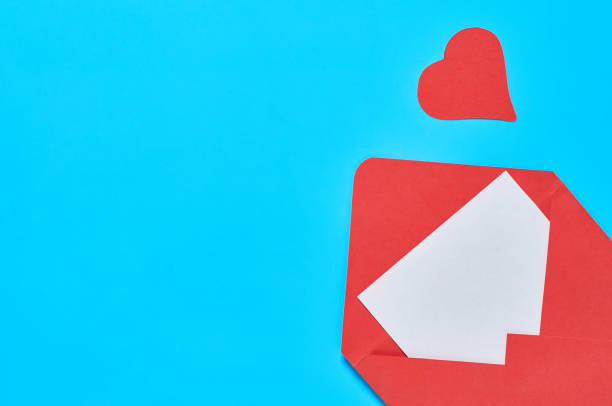 istock Red hearts near open postal envelope with blank white paper on blue desk. Love message. Concept of Valentines Day. Space for text. Top view 1201454248
