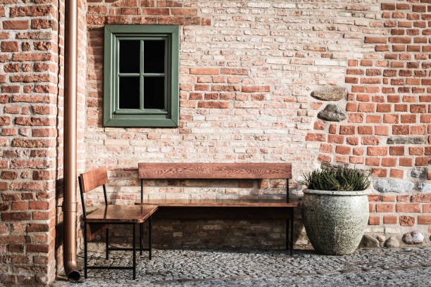 istock Empty bench in brick wall corner with small window. Vintage styles photography. Place inviting on rest. 1201456551