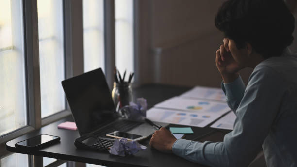 Young businessman giving concentrate on black blank screen laptop after he has feeling disappointed from boss complaining at the working desk over modern office background.