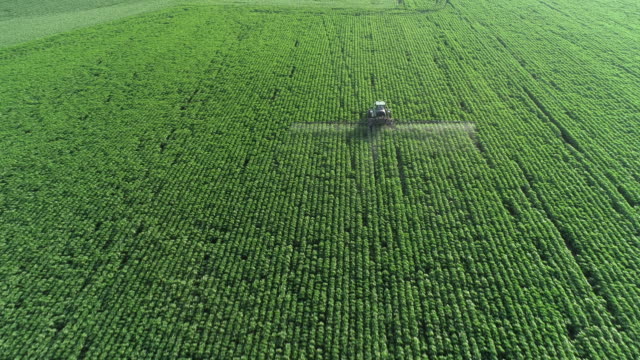 Taking care of the Crop. Aerial view of a Tractor fertilizing a cultivated agricultural field.