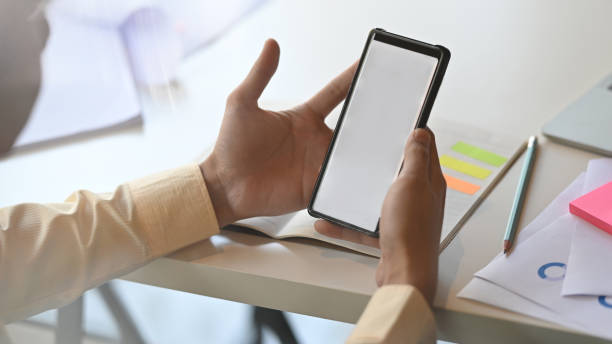 istock Close-up image of young creative man is holding crop black smartphone with white blank screen on working desk. 1201456858