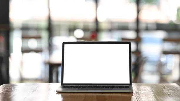 istock Front shot of modern laptop with white blank screen display setting on the wooden table over the blurred modern cafe. 1201456914