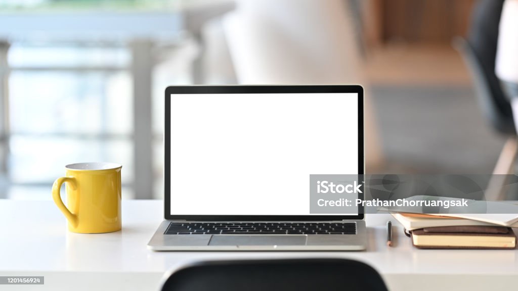 Laptop with white blank screen display and office equipment are putting on the white office desk over the modern office background. Laptop Stock Photo