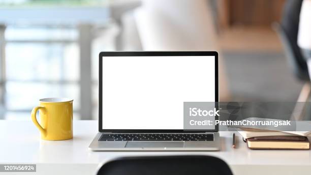Laptop With White Blank Screen Display And Office Equipment Are Putting On The White Office Desk Over The Modern Office Background Stock Photo - Download Image Now