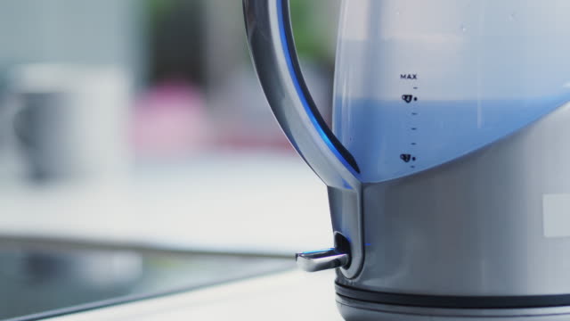 Close Up Of Woman Pressing Power Switch To Boil Electric Kettle At Home