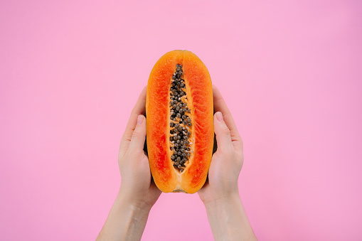 Female hands hold fresh papaya on pink background. Minimalism, space for text.