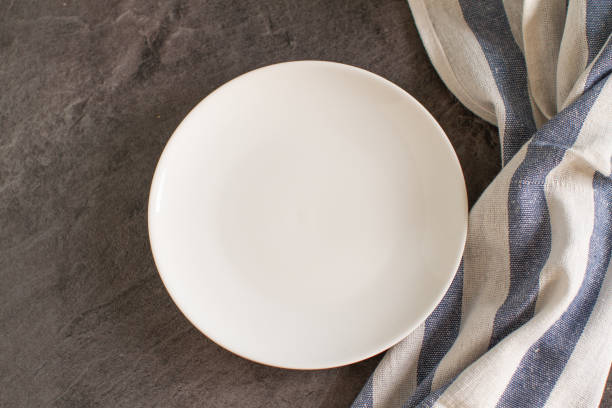 istock White empty plate and blue striped tablecloth on dark background. 1201465640