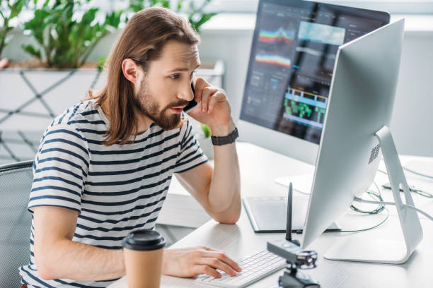istock bearded art editor talking on smartphone near computer monitors 1201466731