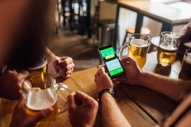 les fans de football méconnaissables buvant de la bière au pub et suivant les résultats des paris en ligne - following photos et images de collection