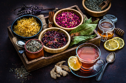 Herbal tea. High angle view of a variety of dried herbs for preparing healthy detox infusions. A cup of tea is at the bottom right. The composition includes dried part of plants like Hibiscus, Calendula, rose petals, green tea, bay leaves, cinnamon sticks, a honey jar, ginger, lemon slices and star anise among others. High resolution 42Mp studio digital capture taken with Sony A7rii and Sony FE 90mm f2.8 macro G OSS lens