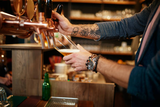 Tattooed caucasian barman pouring beer while standing in pub.