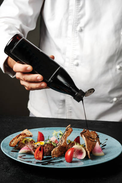 istock Chef plating up food in a restaurant pouring a balsamic sauce over beef tartare before serving it to the customer, close up view of his hand 1201473709