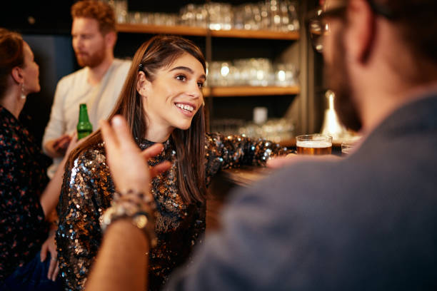 rear view of handsome caucasian man leaning on bar counter, drinking beer and flirting with woman he just met. pub interior. - beer pub women pint glass imagens e fotografias de stock