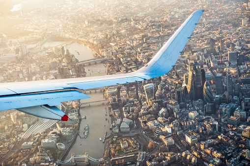 A view of London from a commercial flight, with the towers of London's financial centre, the City of London visible below the wingtip, and Tower Bridge at the bottom of the image.