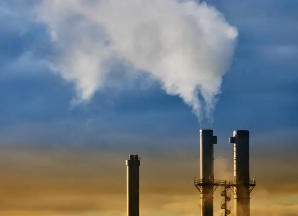 Cloud of steam and smoke from an incinerator chimney in front of a yellow and blue sky