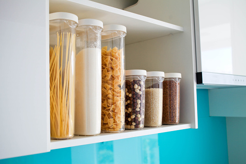 Stocked kitchen pantry with food - pasta, buckwheat, rice and sugar , side view. The organization and storage in kitchen of a case with grain in plastic containers.