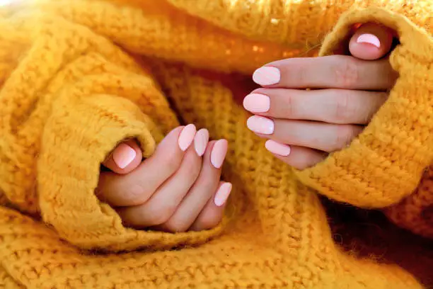 Beautiful female oval shaped pink manicure in an orange sweater. Pink caramel nails, gel polish.