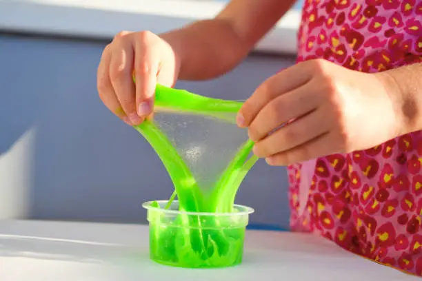 Hand holding homemade toy called Slime, kids having fun and being creative by science experiment. Close up of a little girl is hand playing a green slime